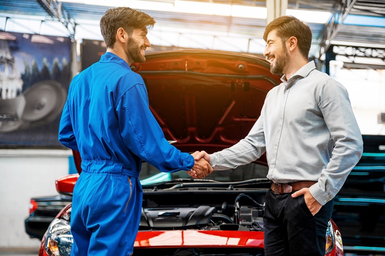 mechanic and customer shaking hands in front of open hood